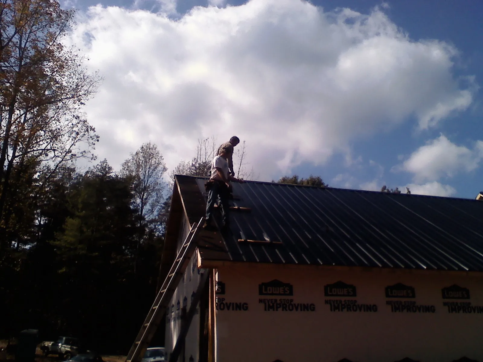 Roofer fastening dark metal panels high against a cloudy sky, from a Roof Inspection job in Athelstane