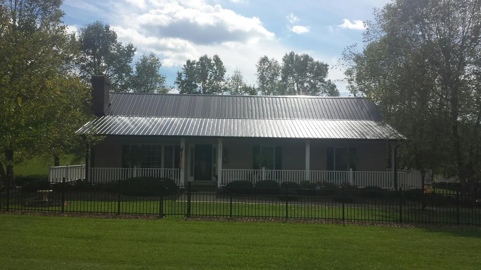 Gray metal roof on a brick ranch with a full width front porch — Gutter Guard Installation work by our crew in Athelstane