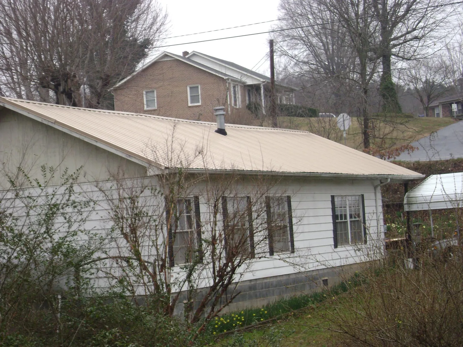 Tan metal roof on a white sided house set into a hillside — Commercial Roofing by Roofing Brothers in Athelstane