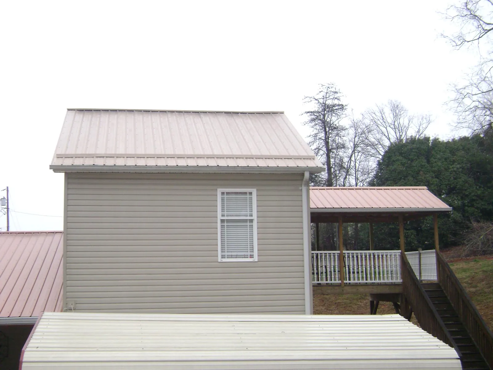 Tan metal roofs on a two story addition and attached porch, from a Roof Replacement job in Athelstane